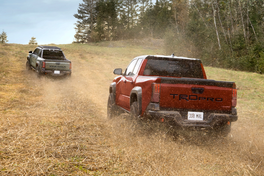 Two Toyota Tacomas driving up a hill. red and black Toyota Tacoma